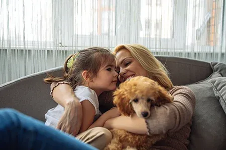mother and daughter holding dog on couch